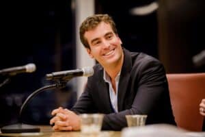 MC Fireside Chats host, in a suit, sitting at a table in front of microphones for the show's episode on January 11, 2023.
