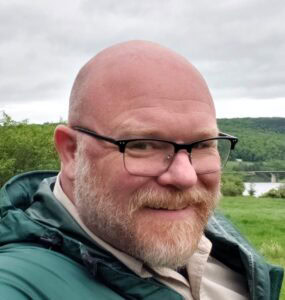 On July 26th, 2023, a bald man in a green jacket captures the moment by taking a selfie during the MC Fireside Chats.