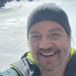 On July 26th, 2023, a man in a beanie is taking a selfie on top of a snowy mountain during MC Fireside Chats.
