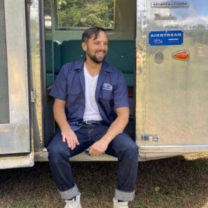 On September 27th, 2023, a man indulges in MC Fireside Chats while comfortably seated in the door of an airstream trailer.