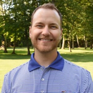 A man in a striped shirt smiling in a park during the MC Fireside Chats on November 8th.