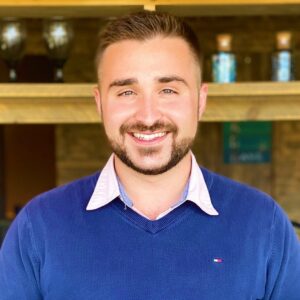 A man smiling in front of a bar, ready to engage in MC Fireside Chats.