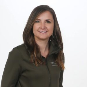 A woman in a green jacket smiles in front of a white background during the January 31st episode of MC Fireside Chats.