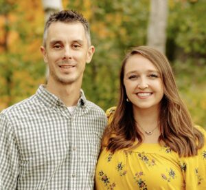 A man and woman posing in front of trees at the MC Fireside Chats on January 31st, 2024.