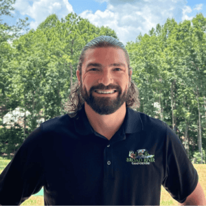 Man with a beard smiling outdoors wearing a black polo shirt with "broad river campground" logo, captured on March 20th.