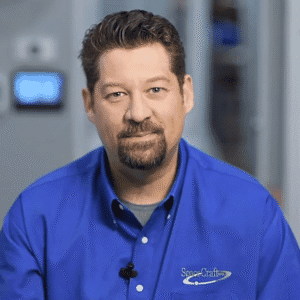 A man wearing a blue shirt with a "Space Crafts" logo, seated indoors, looking at the camera, with a blurred background showing part of a room and a digital device on the wall. The scene hints at an upcoming MC Fireside Chats session on May 22nd, 2024.